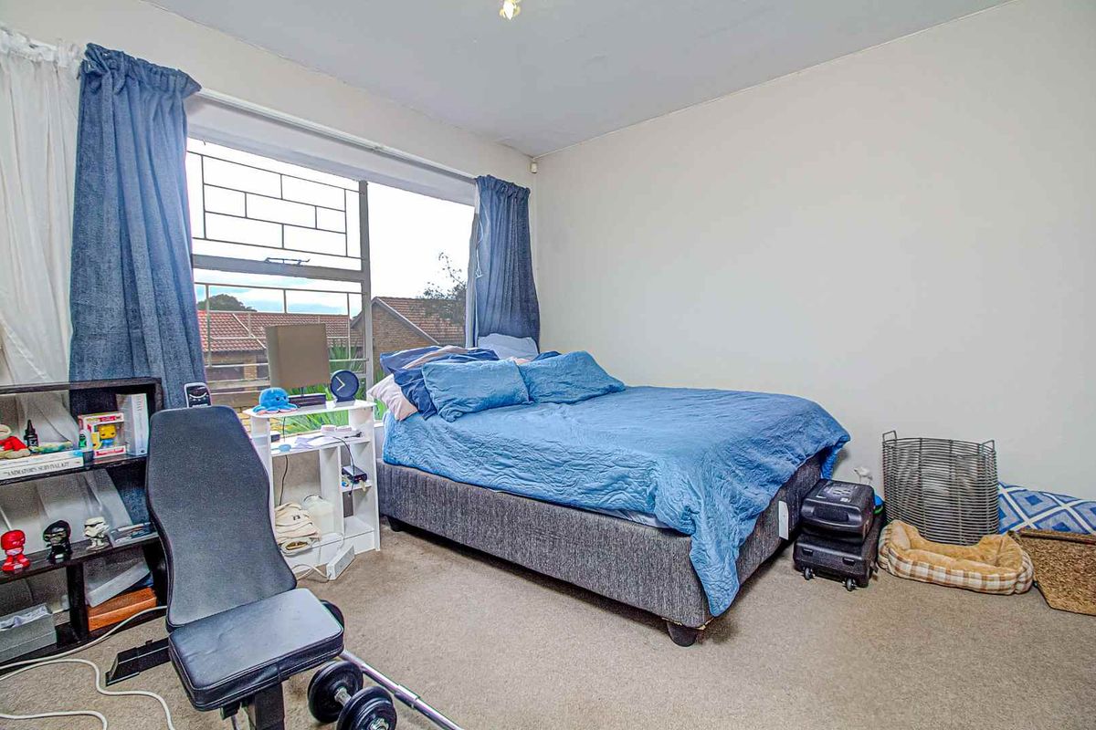 A standard bedroom featuring a large window with security bars, neutral wall finishes, and carpeted flooring.