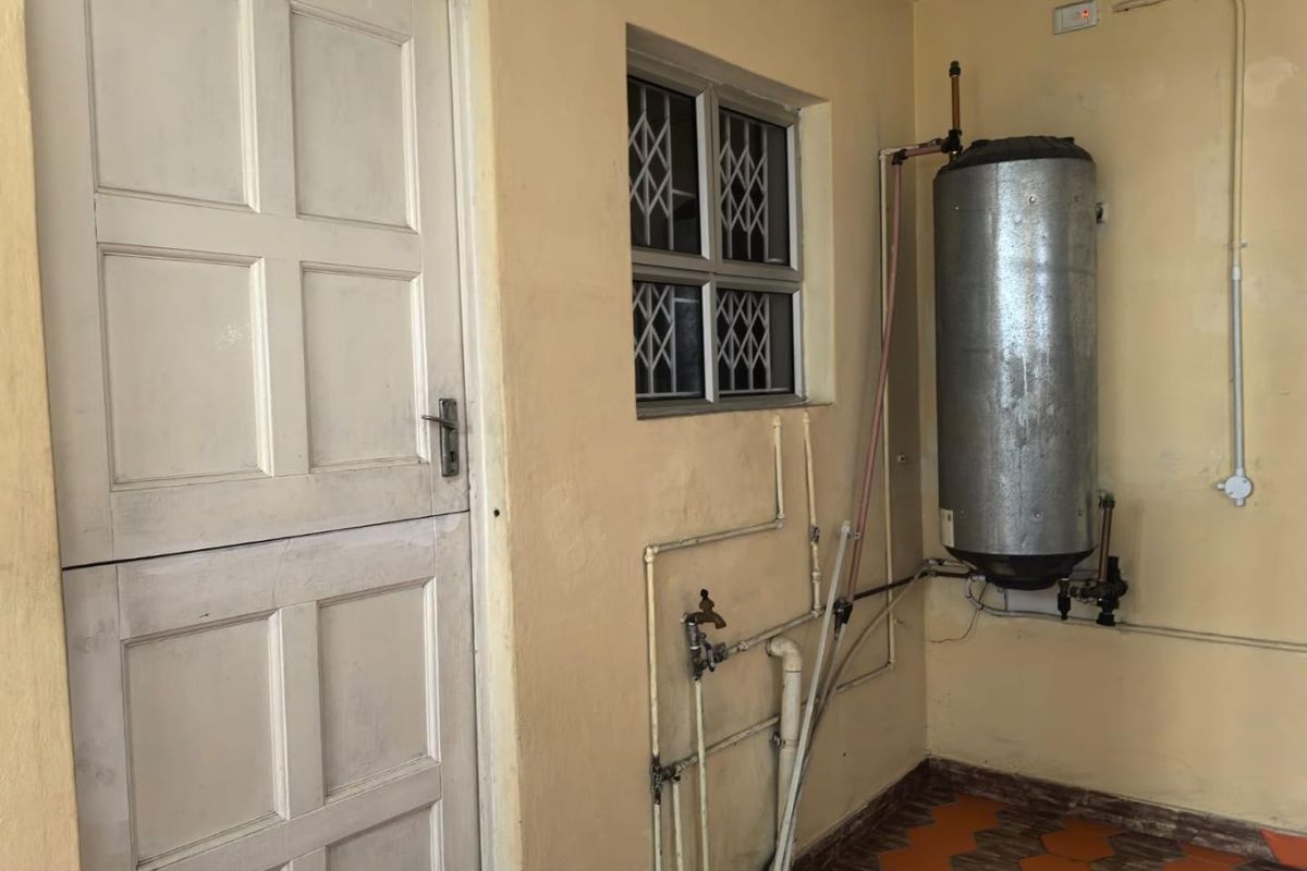 Utility area featuring an electric water heater, exposed plumbing, and tiled flooring, providing functional space for laundry or storage needs.