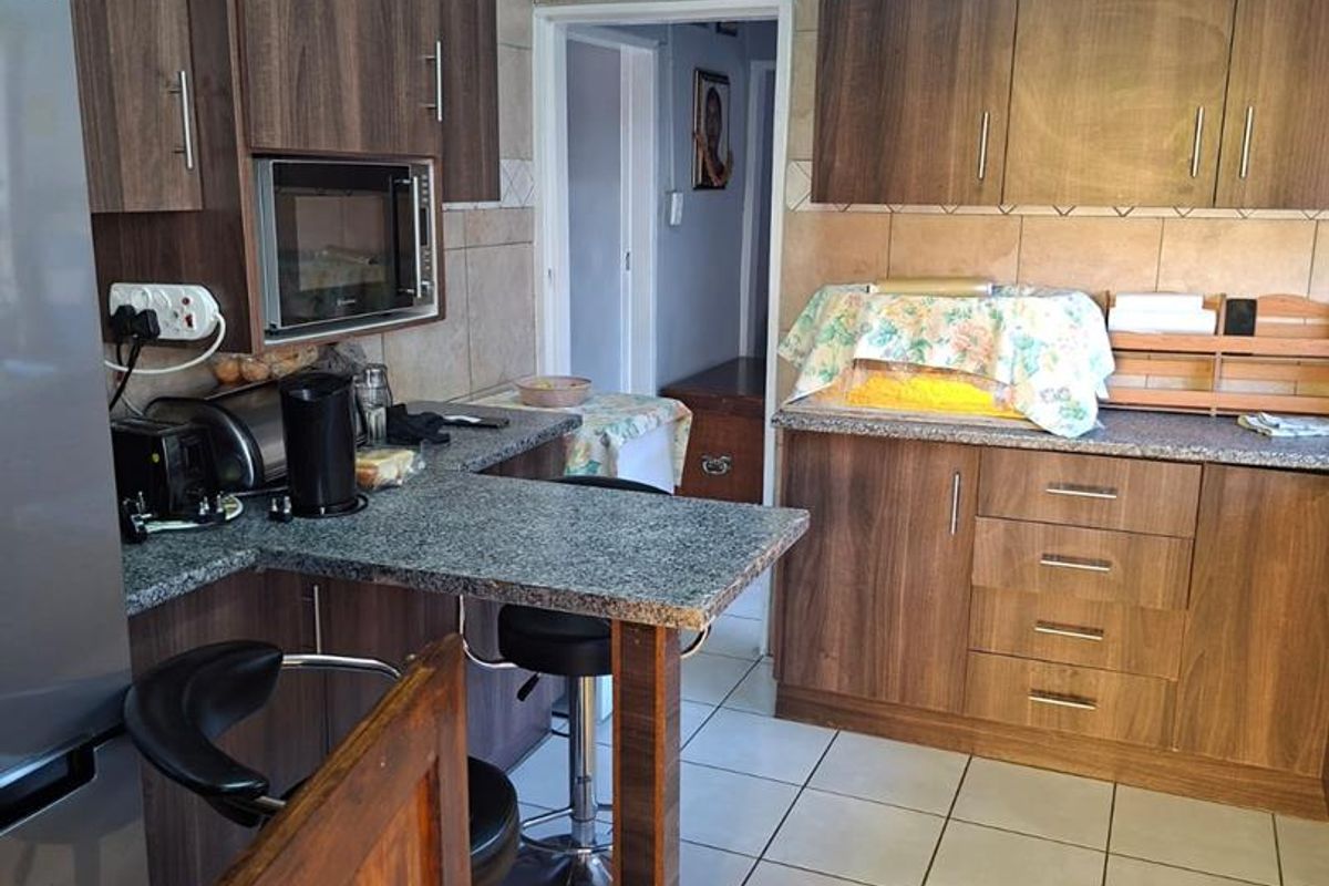 Functional kitchen featuring wood-look cabinetry, granite-style countertops, tiled backsplash, and ceramic floor tiles with a breakfast bar area.