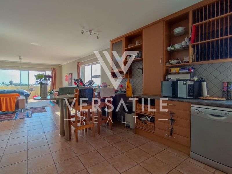 Open-plan living area featuring a kitchen with built-in cabinetry and tiled flooring, leading to a balcony with natural light.