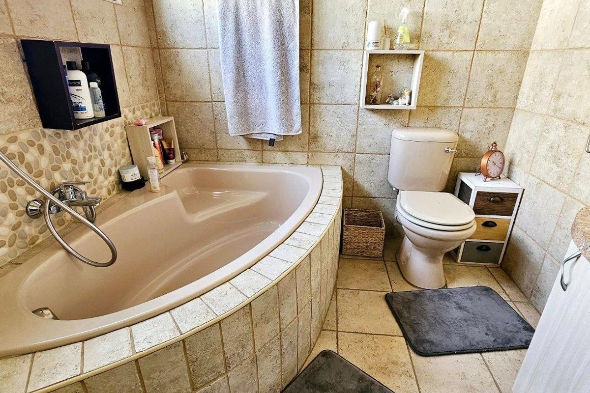 A functional bathroom featuring a built-in corner bathtub, toilet, and neutral tiled finishes throughout.
