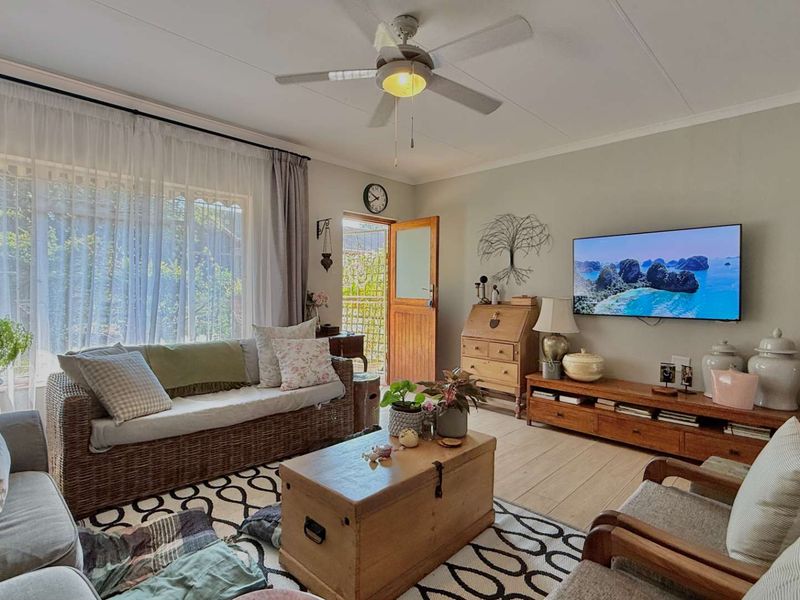 A comfortable living room featuring laminate flooring, a ceiling fan, and direct access to the exterior through a secure timber door.
