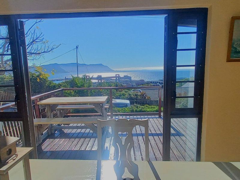 Living area featuring large glass sliding doors opening onto a timber deck with expansive coastal and mountain views.