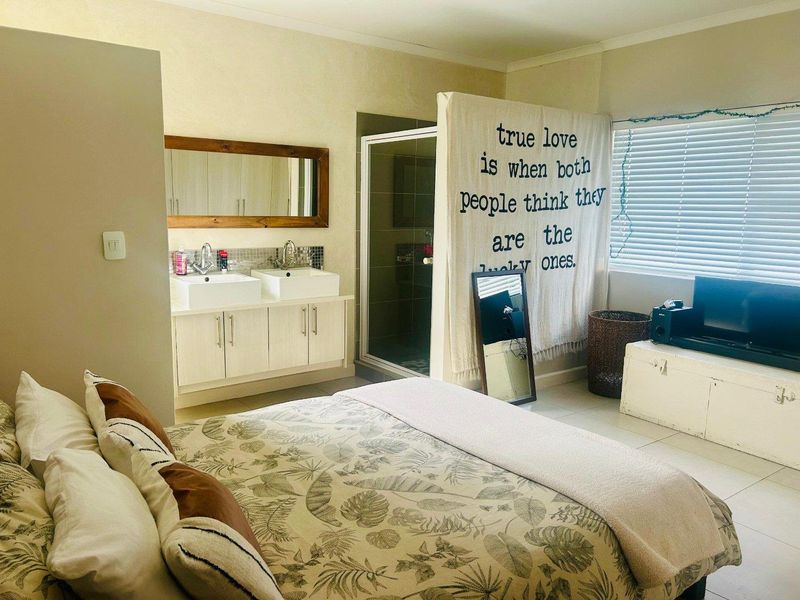 Spacious bedroom featuring an integrated en-suite bathroom with a double vanity and glass-enclosed shower, complemented by neutral tiled flooring and natural light.