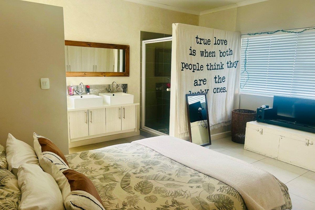 Spacious bedroom featuring an integrated en-suite bathroom with a double vanity and glass-enclosed shower, complemented by neutral tiled flooring and natural light.