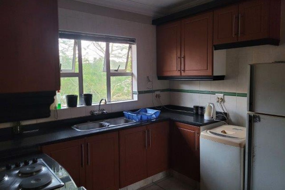 A functional kitchen featuring dark wood-look cabinetry, laminate countertops, a double basin sink, and an integrated electric hob with tiled backsplash.