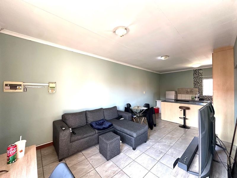 Open-plan living area featuring tiled flooring, a functional kitchen with cabinetry and a breakfast counter, and neutral wall finishes.