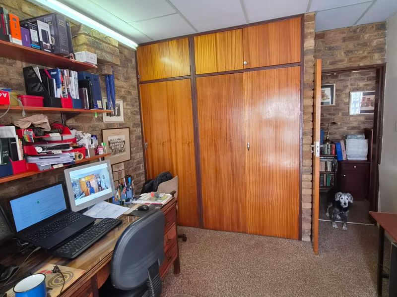Bedroom featuring exposed brick walls, built-in wooden cupboards, and carpeted flooring, offering a functional space with potential for modernization.