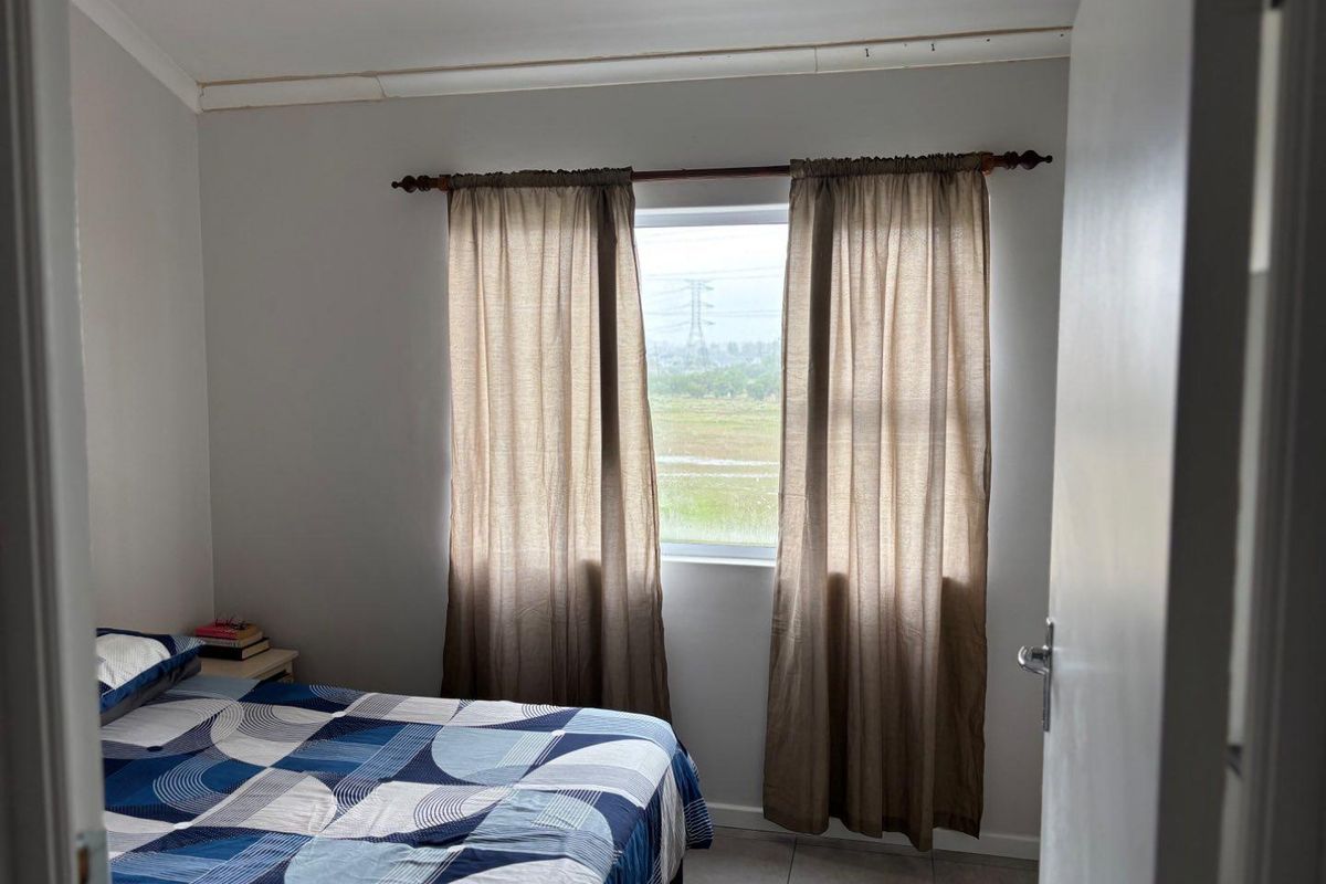 A simple bedroom featuring tiled flooring and a window with natural light, providing a functional space for rest.