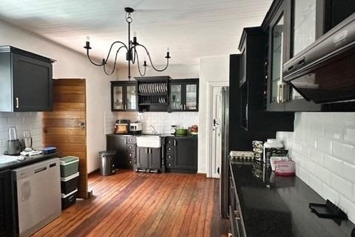 Spacious kitchen featuring black cabinetry, granite countertops, subway tile backsplash, farmhouse sink, and original timber flooring and ceiling.