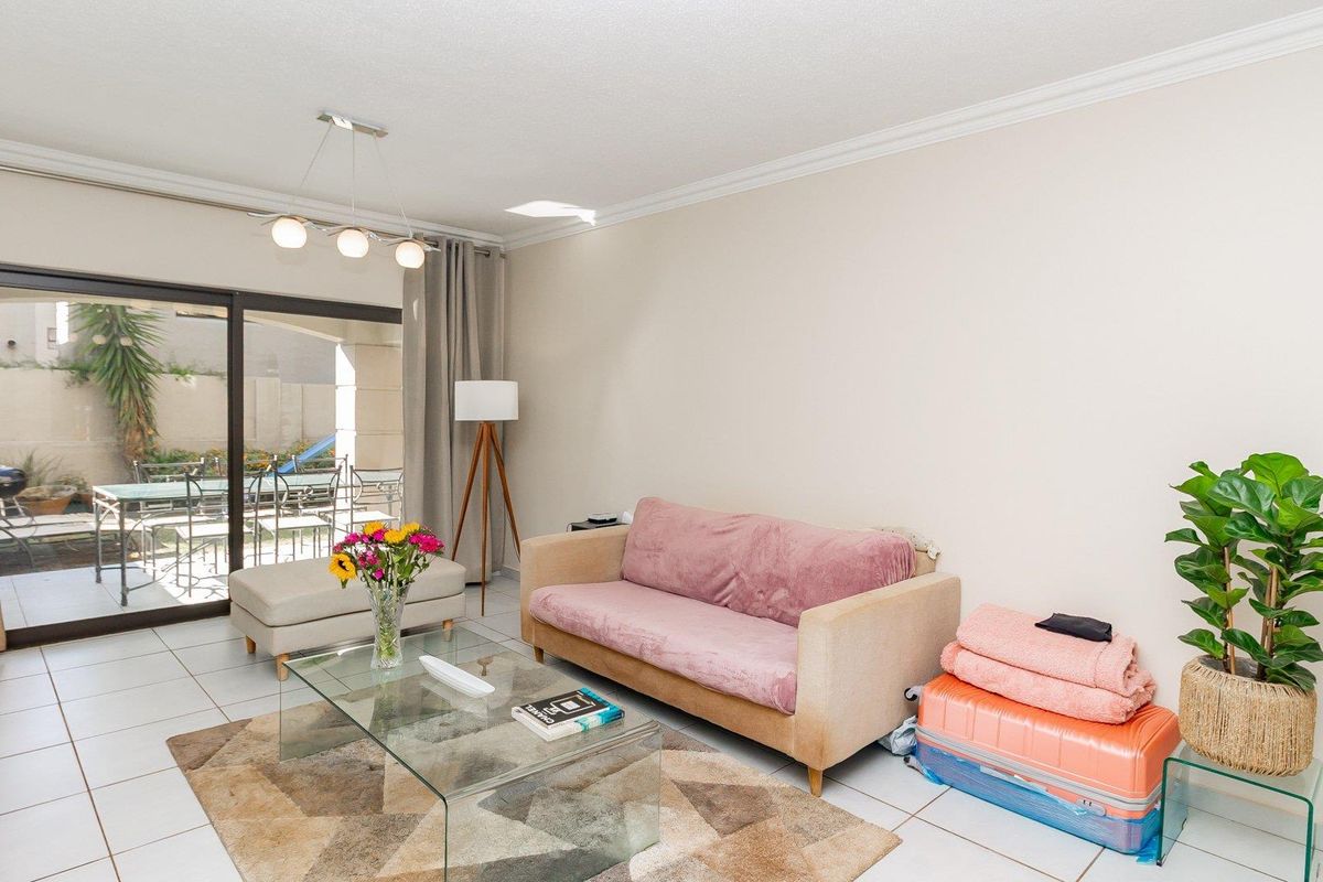 A bright living room featuring tiled flooring, cove cornicing, and a large sliding glass door providing direct access to the outdoor patio area.