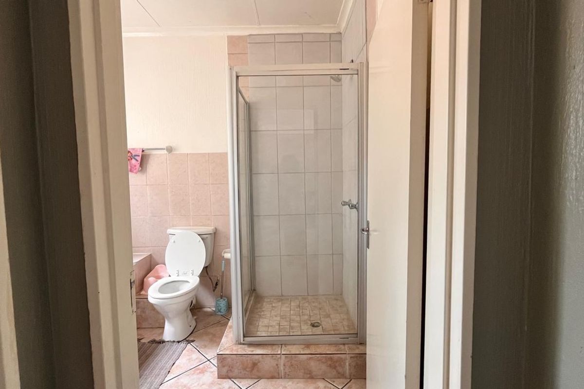 A functional bathroom featuring a walk-in shower enclosure with tiled base and a standard toilet, requiring cosmetic updates to modernize the space.