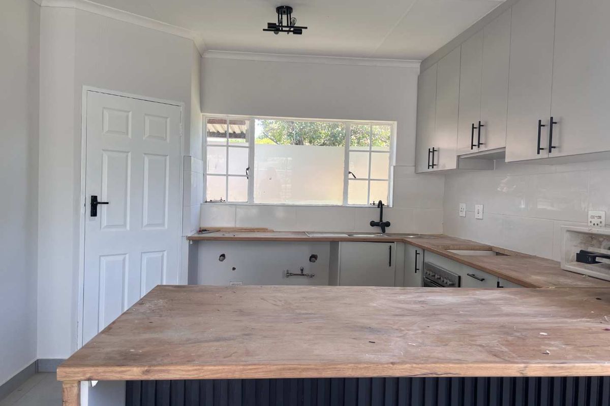 A kitchen featuring light-toned cabinetry, a wooden breakfast bar, and a window overlooking the exterior, currently awaiting final installation and finishing touches.