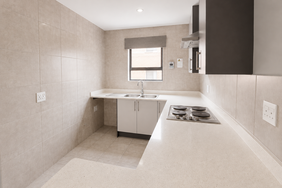 A modern, clean kitchen featuring neutral tiled walls, stone countertops, built-in cabinetry, an electric hob, and a double sink with a window view.