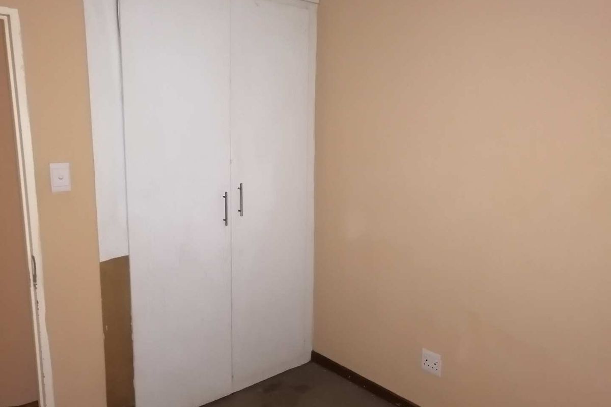 A vacant bedroom featuring a built-in cupboard, requiring cosmetic updates to the wall finishes and flooring to improve its overall condition.