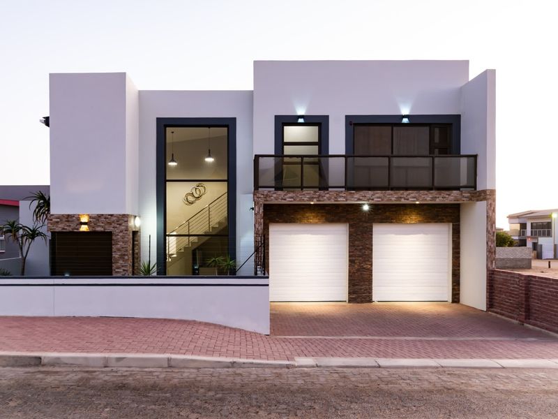 Modern double-story residence featuring a double garage, stone-clad accents, a private balcony, and a paved driveway with contemporary exterior lighting.