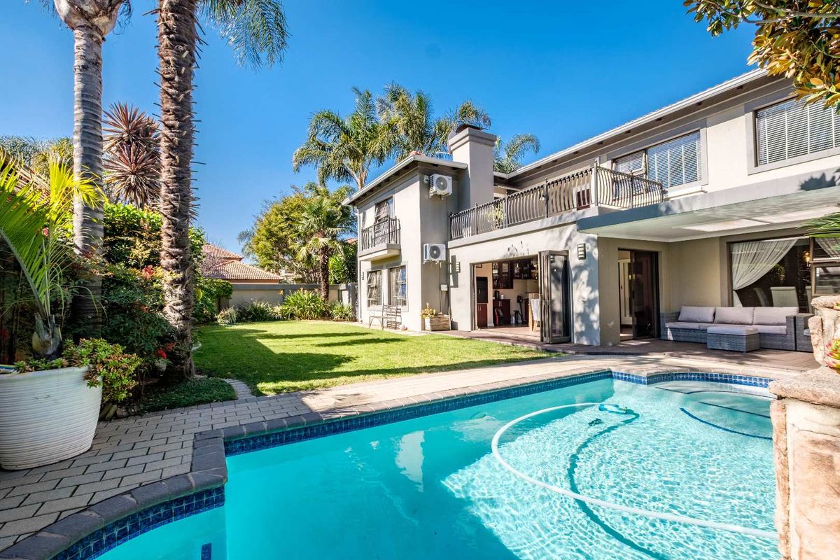 Rear view of the property featuring a swimming pool, manicured lawn, paved patio area, and a balcony overlooking the garden.