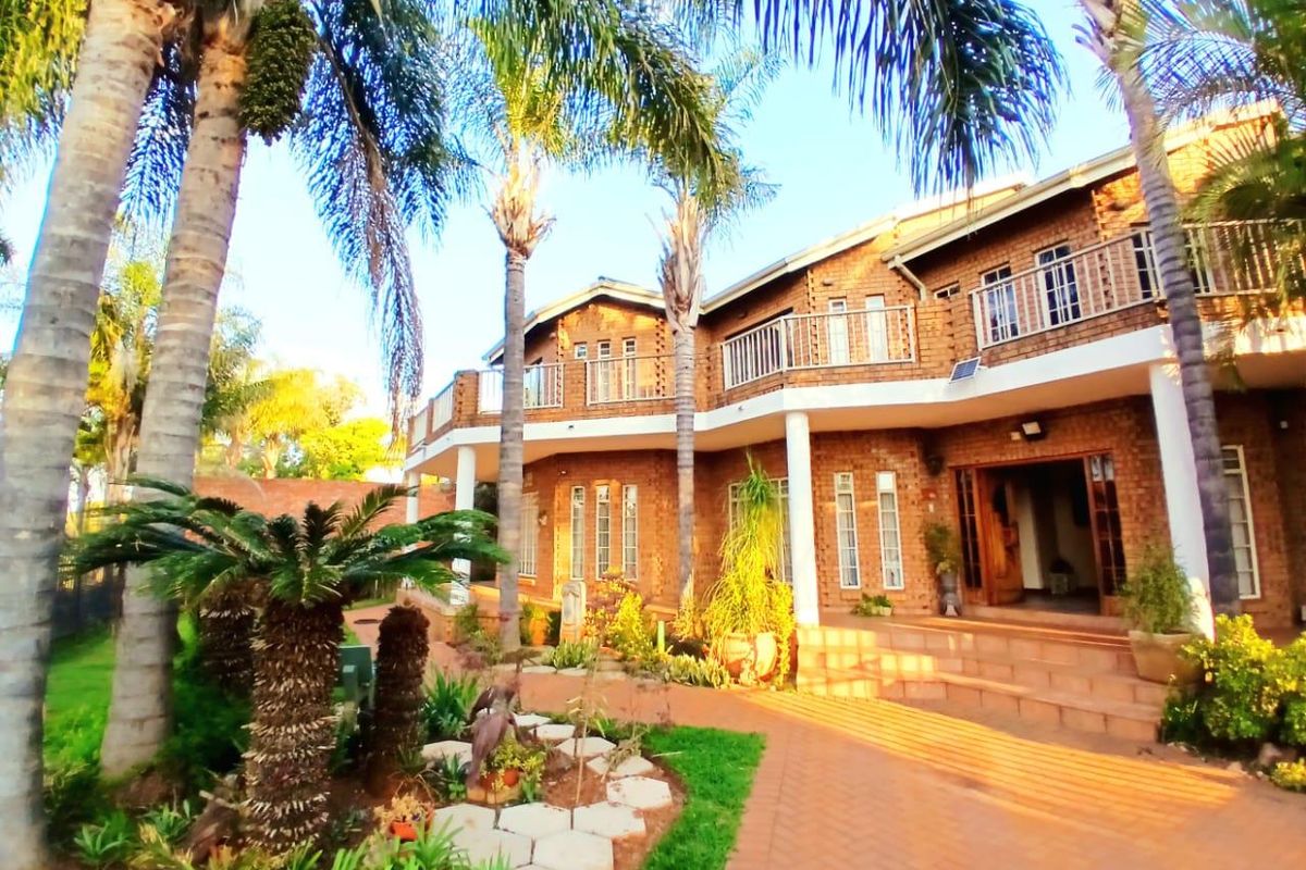A spacious double-story face brick home featuring an expansive paved patio, upper-level balcony, and established landscaped garden.