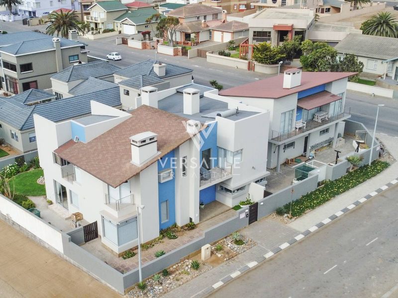 Aerial view of a modern residential property featuring a tiled roof, multiple chimneys, balconies, and a well-maintained garden with boundary walls.