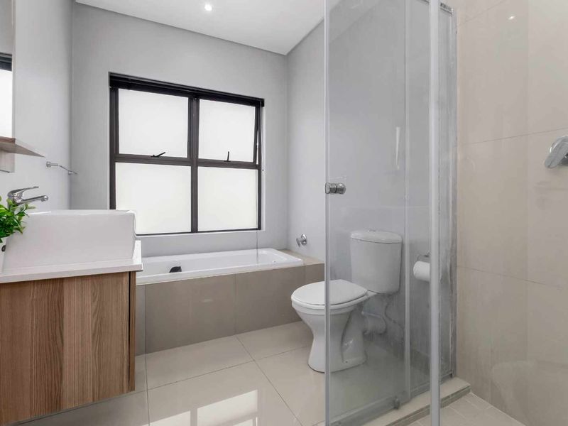 Modern bathroom featuring a vessel sink vanity, built-in bathtub, and a separate glass-enclosed shower with neutral tiling throughout.