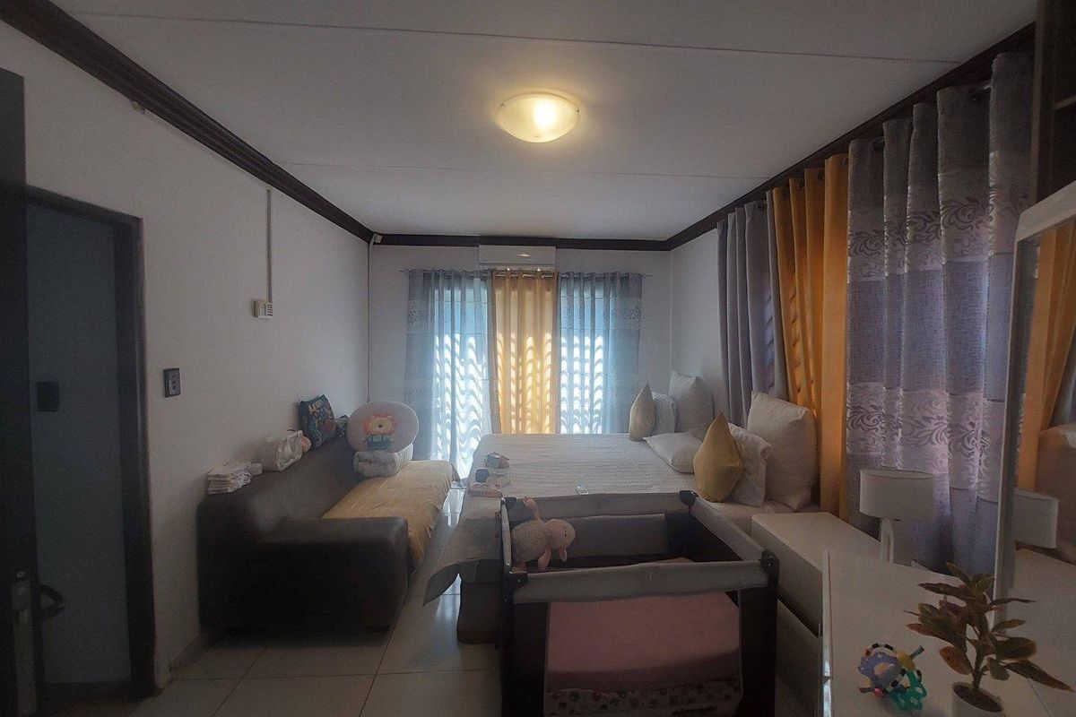 A bedroom featuring tiled flooring, a wall-mounted air conditioning unit, and large windows with curtains.
