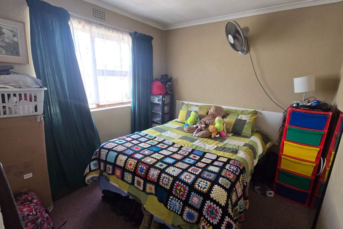 A standard bedroom featuring a wall-mounted fan and a window with curtains, providing a functional living space.