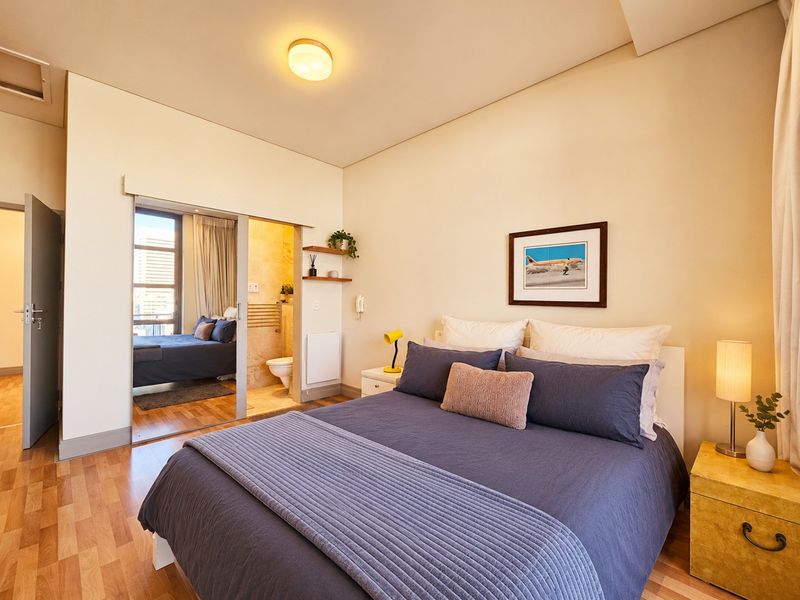 A well-maintained bedroom featuring laminate flooring, a sliding door leading to an en-suite bathroom, and built-in shelving.