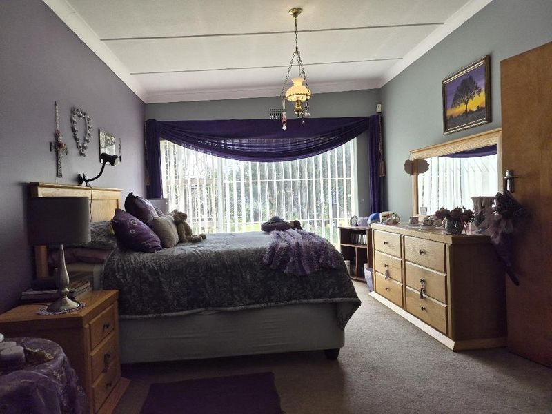 A spacious bedroom featuring carpeted flooring, coved ceilings, and large vertical blinds allowing natural light.