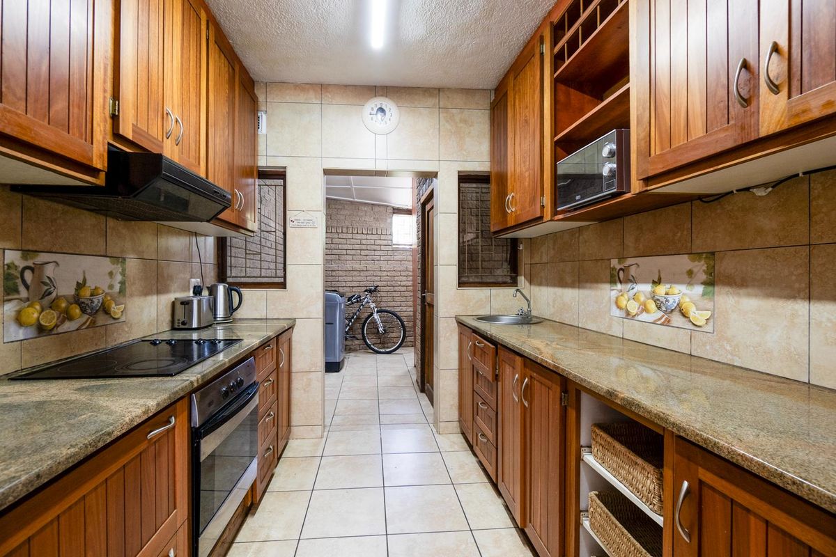 Galley-style kitchen featuring timber cabinetry, granite countertops, integrated oven and hob, and tiled flooring, leading through to a utility area.