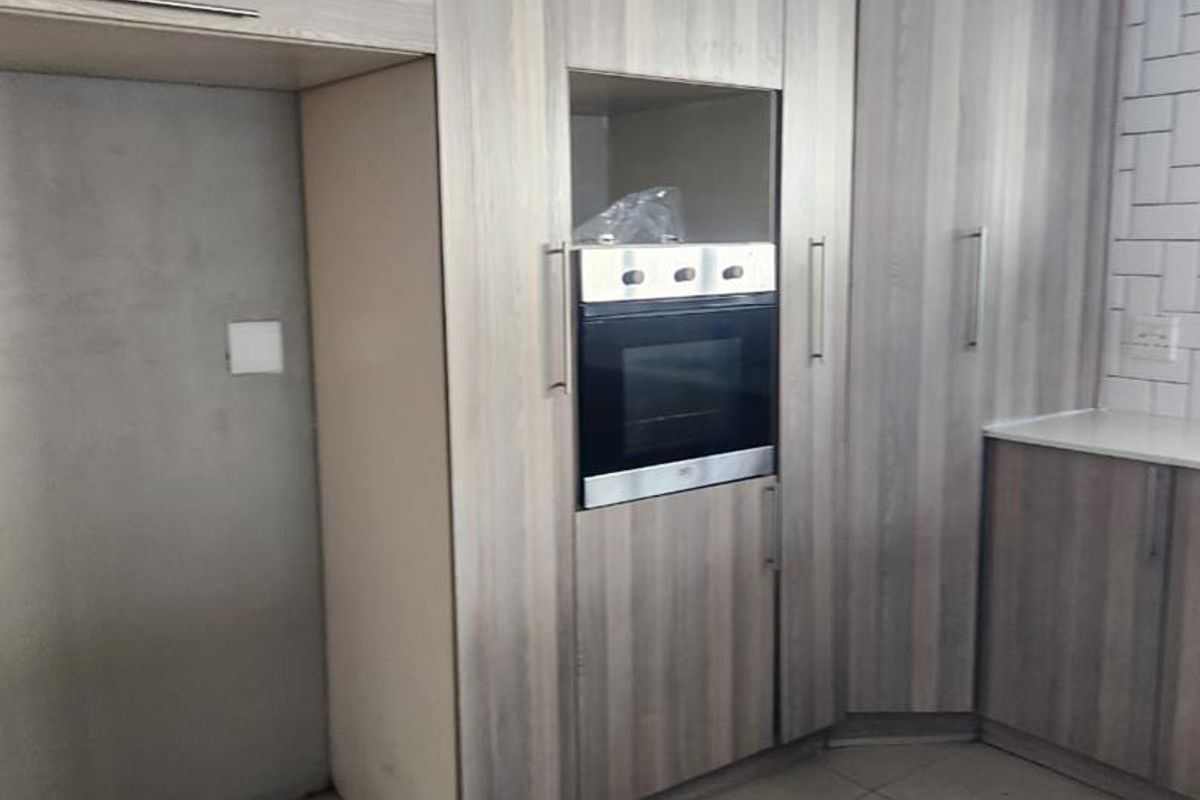 A kitchen area featuring modern wood-look cabinetry, a built-in oven, and a tiled backsplash, currently awaiting final finishes and appliance installation.