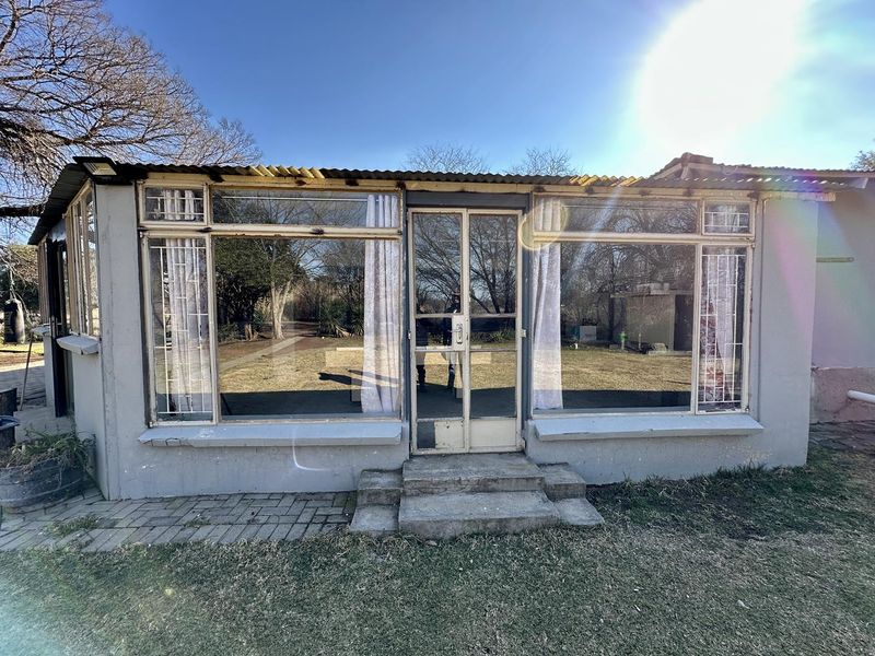 Rear exterior view of a small holding structure featuring large glass windows, a metal door, and a corrugated iron roof.