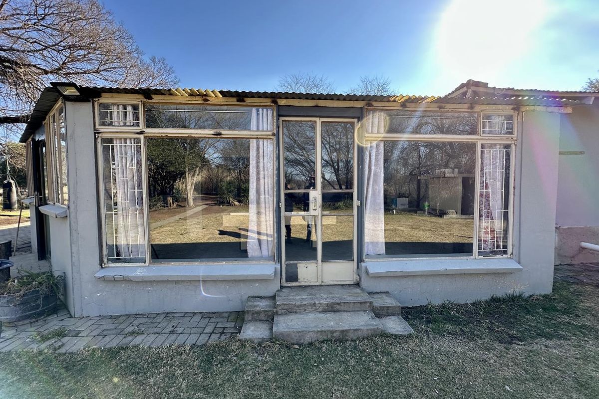 Rear exterior view of a small holding structure featuring large glass windows, a metal door, and a corrugated iron roof.
