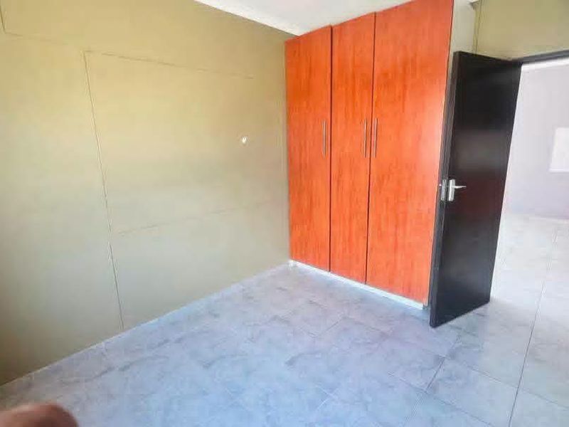 An empty bedroom featuring tiled flooring and built-in wooden cupboards, with a view into an adjacent room.