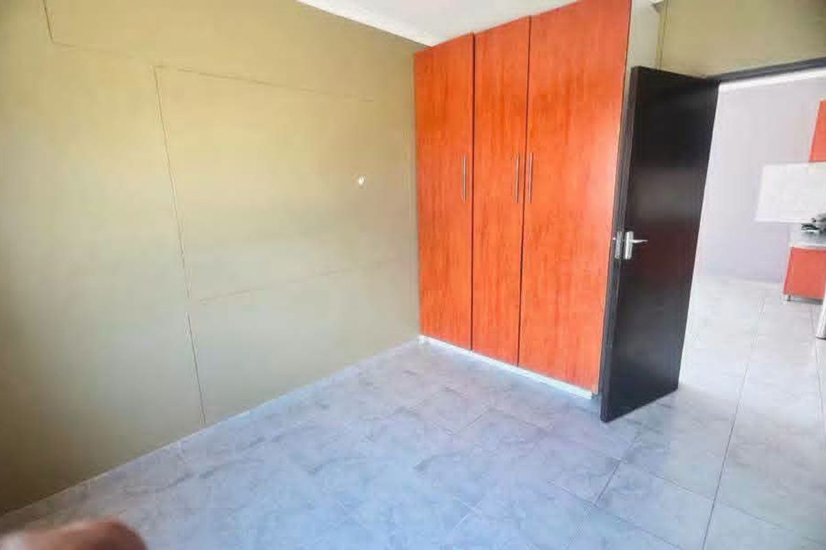 An empty bedroom featuring tiled flooring and built-in wooden cupboards, with a view into an adjacent room.