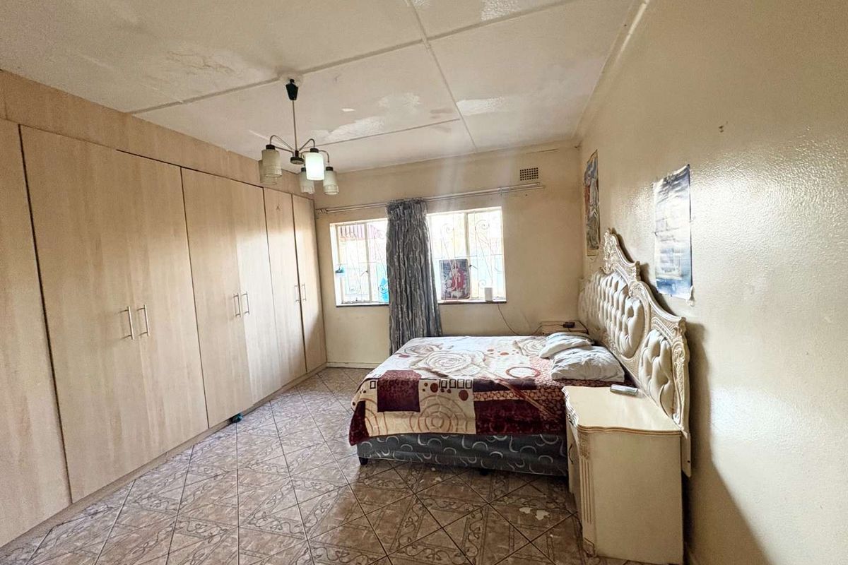 A bedroom featuring built-in cupboards, tiled flooring, and security bars on the windows. The room shows signs of wear and requires maintenance.