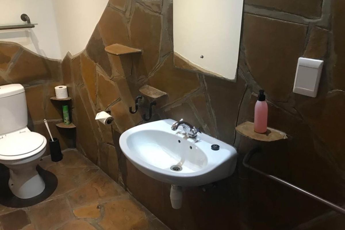 A bathroom featuring rustic stone wall cladding, a wall-mounted basin, a toilet, and integrated stone shelving.