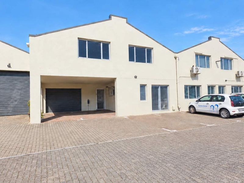 Front elevation of an industrial property featuring paved parking, roller shutter doors, and multiple office windows with exterior air conditioning units.