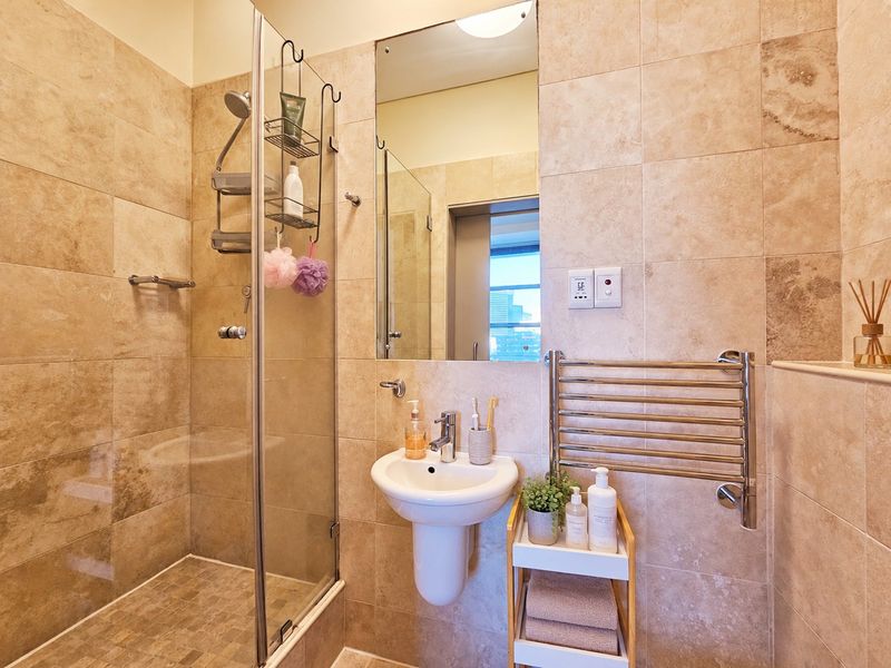 Modern bathroom featuring a glass-enclosed shower, wall-mounted basin, and a chrome heated towel rail, finished with neutral stone-look wall tiles.