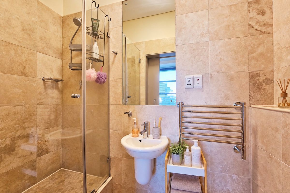 Modern bathroom featuring a glass-enclosed shower, wall-mounted basin, and a chrome heated towel rail, finished with neutral stone-look wall tiles.