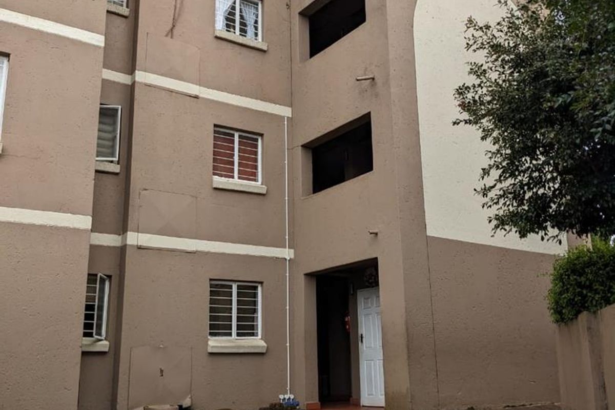 Rear exterior view of a multi-story townhouse complex featuring a paved walkway, small lawn area, and standard window security bars.