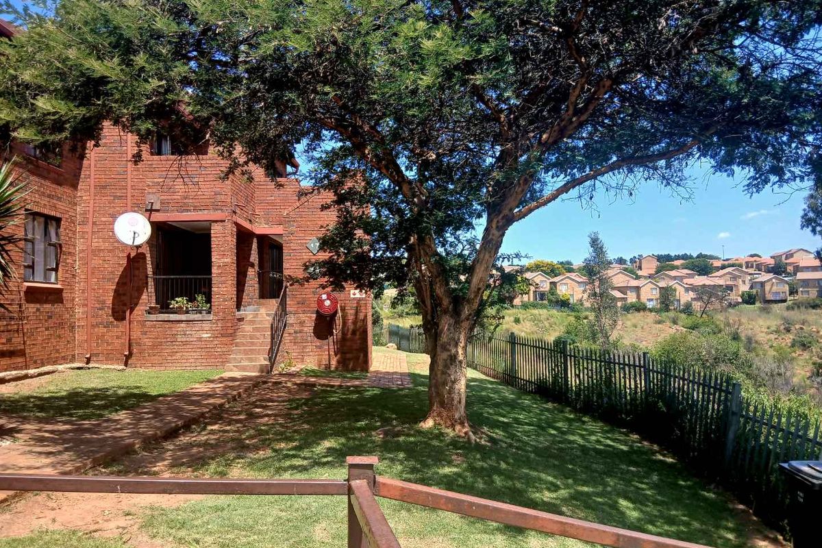 A view of the rear exterior of the townhouse, featuring a brick facade, a private garden area, and perimeter fencing.