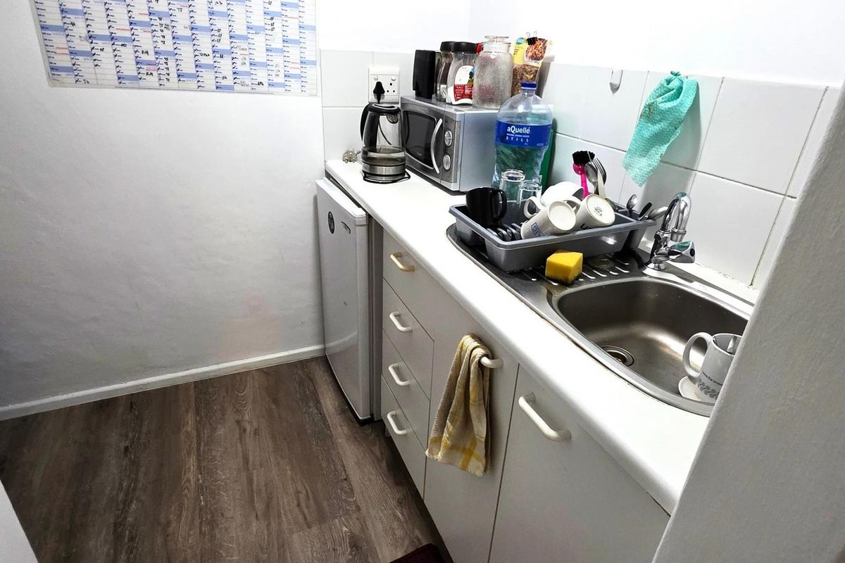 A compact kitchenette area featuring a stainless steel sink, built-in cabinetry, and tiled splashback, suitable for office utility use.