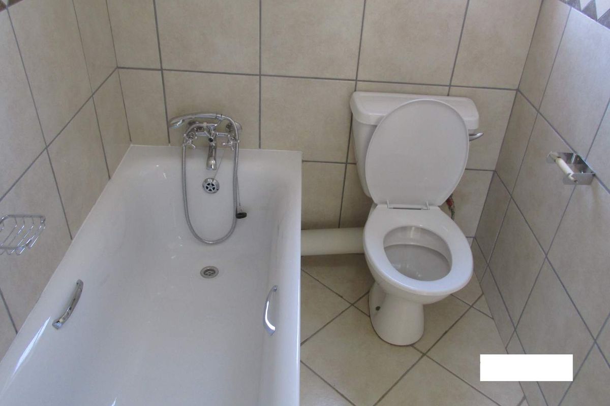 A functional bathroom featuring a standard bathtub with handheld shower attachment and a close-coupled toilet, finished with neutral wall and floor tiling.