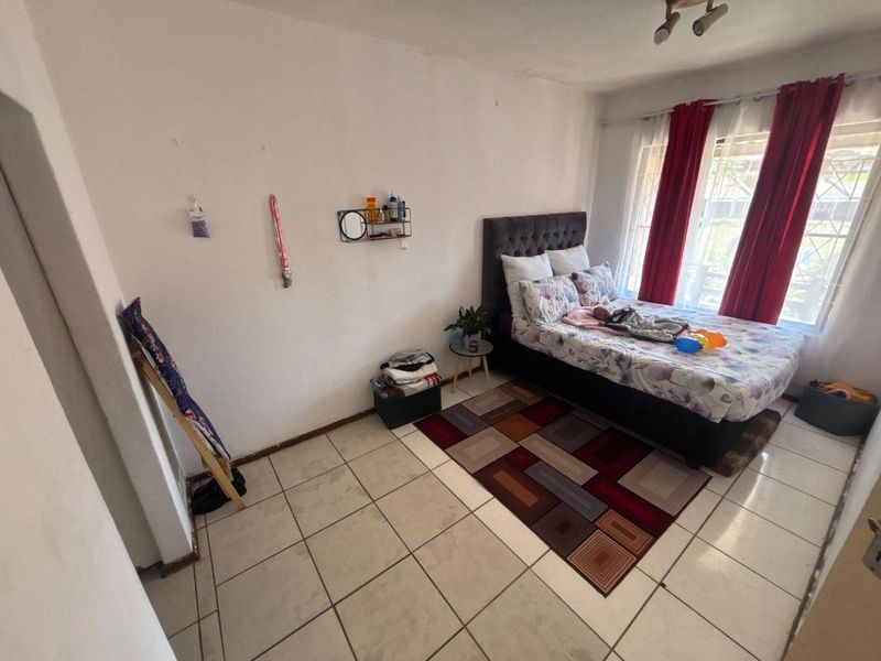A bedroom featuring tiled flooring and a window with security bars, offering a functional space ready for cosmetic updates.