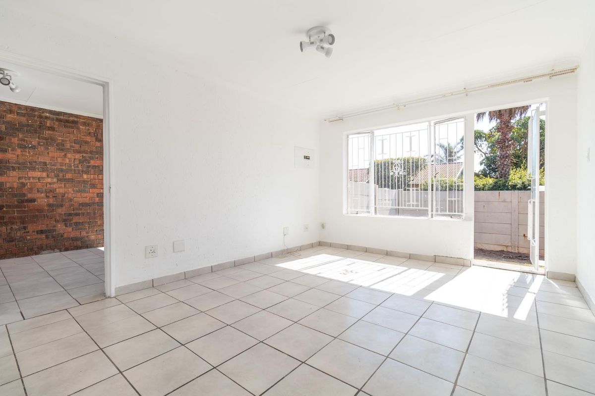 A bright, empty living area featuring tiled flooring, security bars on windows, and direct access to an outdoor space.