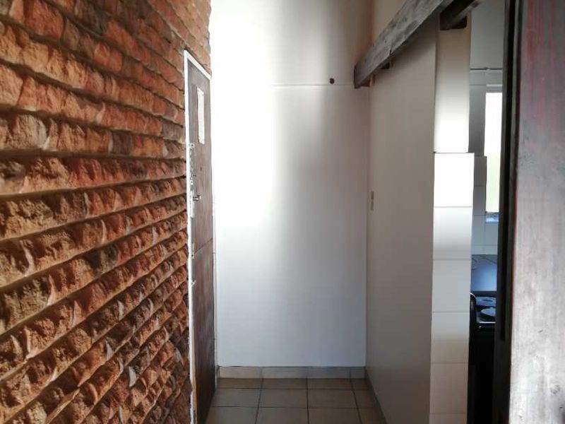 A functional hallway featuring an exposed brick feature wall, tiled flooring, and a timber-paneled ceiling, providing a rustic aesthetic transition between living spaces.