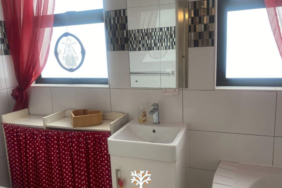 A functional bathroom featuring a vanity cabinet with a ceramic basin, chrome mixer tap, and decorative mosaic tile accents on the wall.