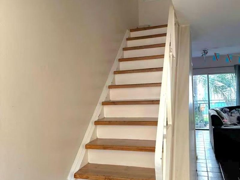 A staircase with wooden treads and a painted balustrade leading to the upper level, adjacent to a tiled living area.