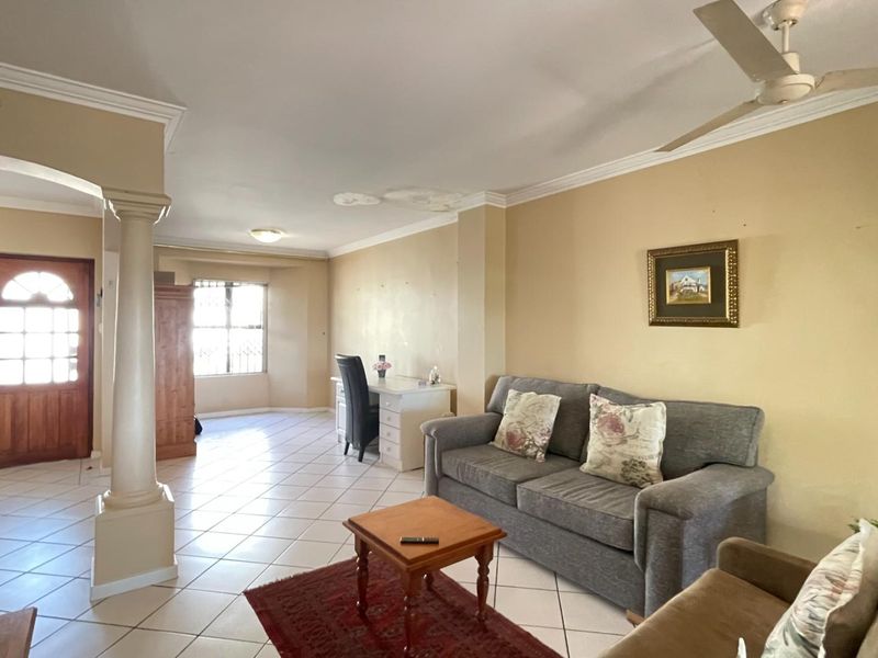 Spacious living area featuring tiled flooring, a decorative column, and a ceiling fan, with visible ceiling water damage requiring attention.