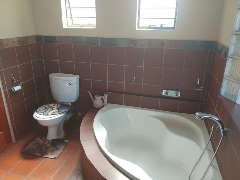 A functional bathroom featuring a corner bathtub, toilet, and tiled finishes with natural light from louver and glass block windows.